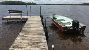 A wooden dock extending into a lake with a boat tied to it and a bench on the dock. - Rustic 2 Bed Lakeside Cabin - boats available (Hayward)