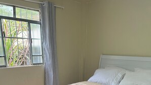 Ein ordentlich bezogenes Bett mit einer beigen und braunen Bettdecke, einer grauen Decke und einem violetten Handtuch.