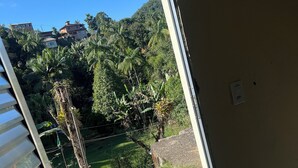 Blick aus einem Zimmer mit großem Fenster auf eine Wiese mit Bäumen und ein Gebäude in der Ferne.