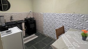 Eine kleine Küche mit Kühlschrank, Herd und Spüle. Ein Esstisch mit Spitzenbeschichtung und ein Topf mit Pflanze.