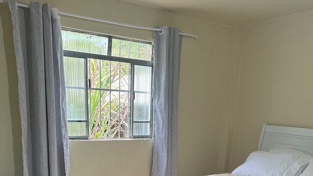 Ein Schlafzimmer mit Bett, einem fensterbelaubten Fenster, einem Teppich und Blick auf grüne Vegetation.