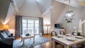 A spacious living room with a high ceiling, a dining area with a table set for four, and a cozy seating area with a sofa and a lamp.