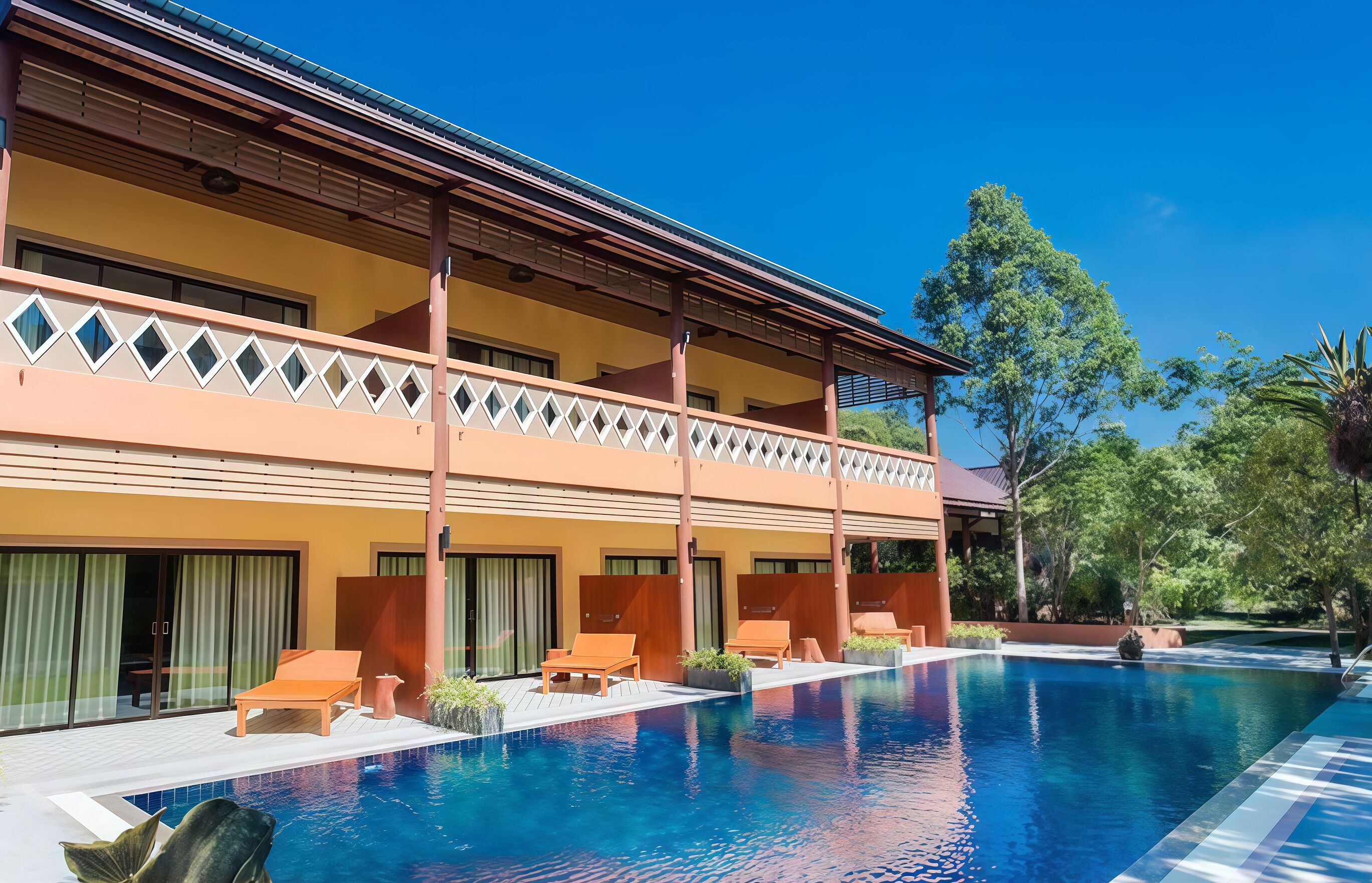 A hotel with a pool, wooden lounge chairs, and a covered balcony area.
