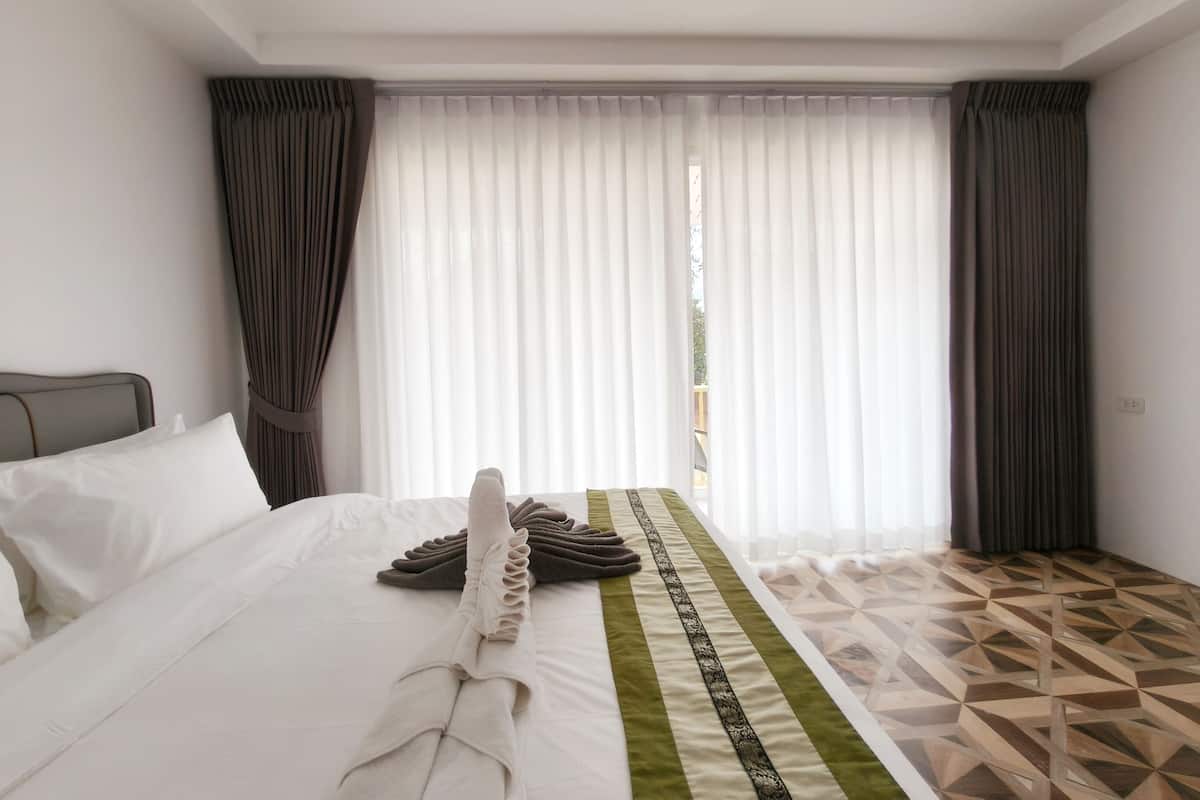 A hotel room with a neatly made bed, a green and black patterned runner, and a geometric patterned floor.
