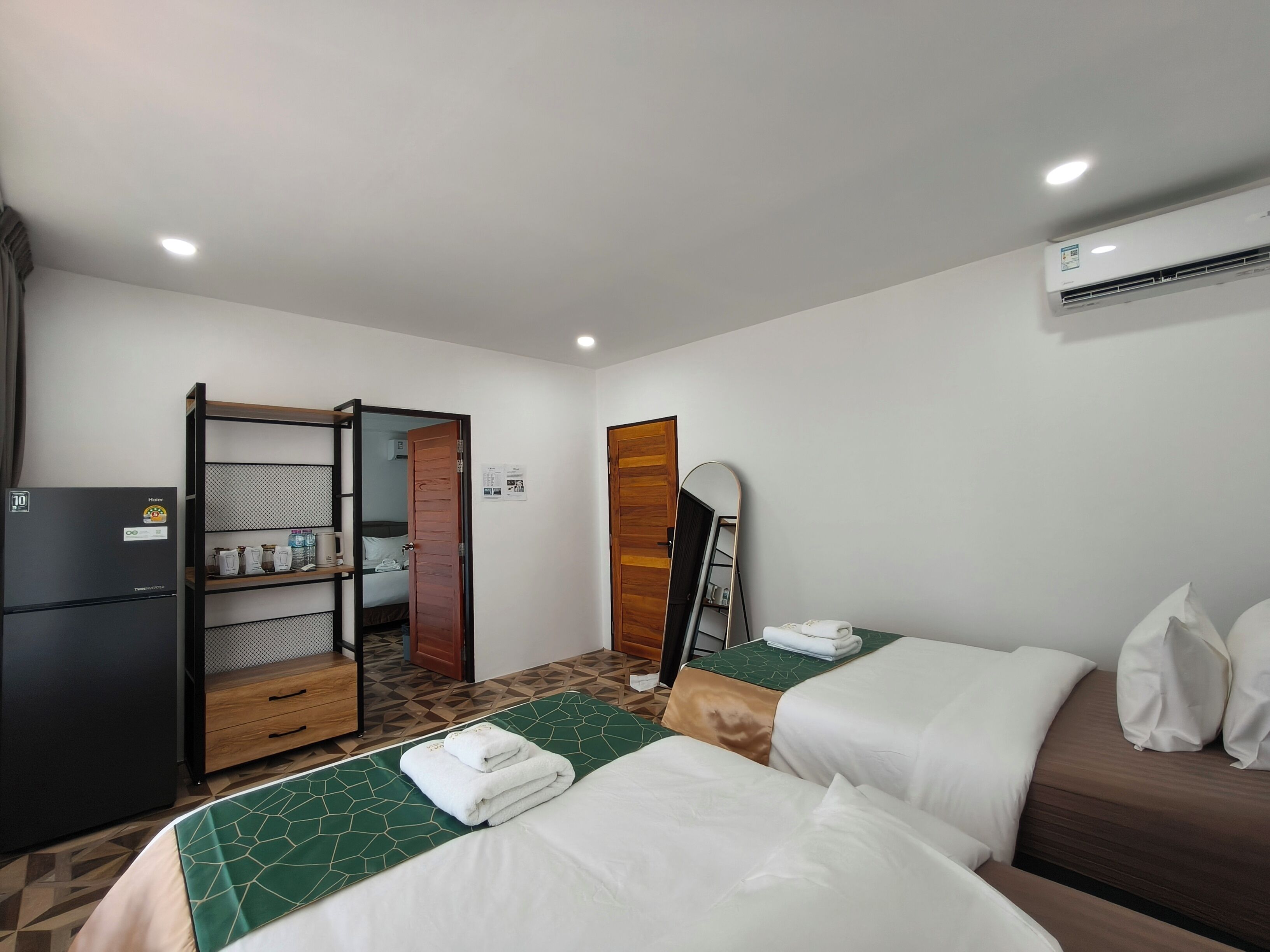A hotel room with two beds, a minibar, a wardrobe, and an air conditioning unit.