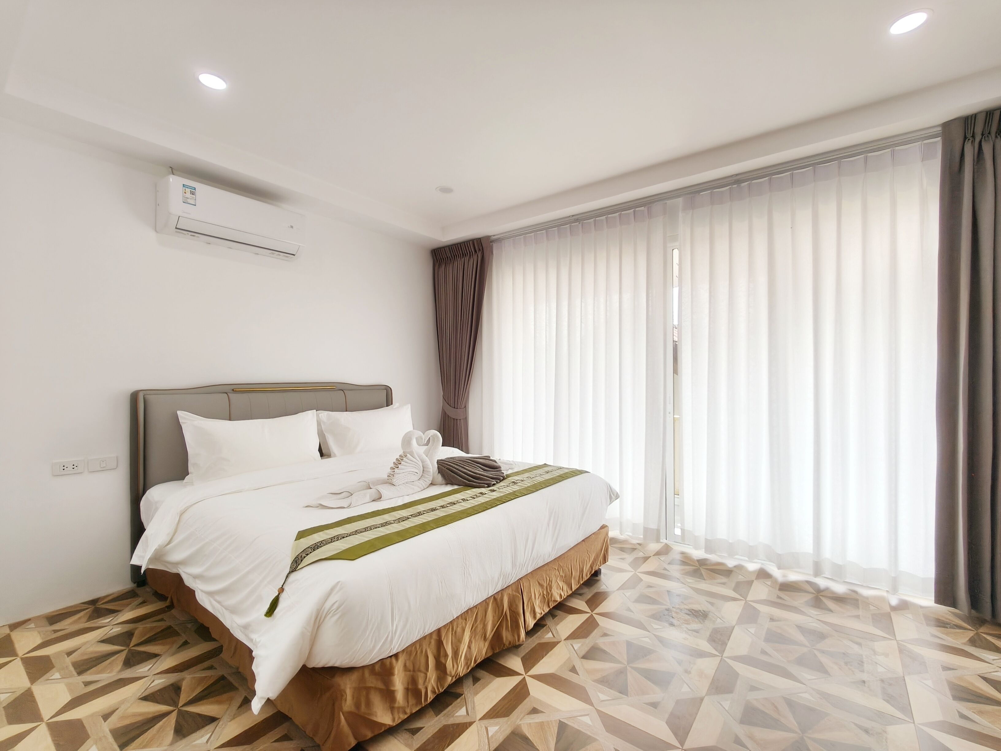 Una habitación de hotel moderna con cama, unidad de aire acondicionado y un gran ventanal con cortinas.