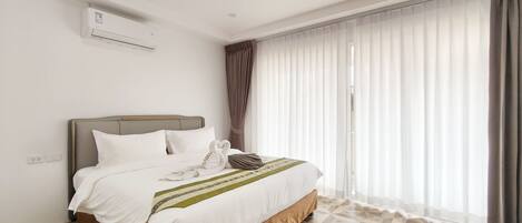 Una habitación de hotel moderna con cama, unidad de aire acondicionado y un gran ventanal con cortinas.