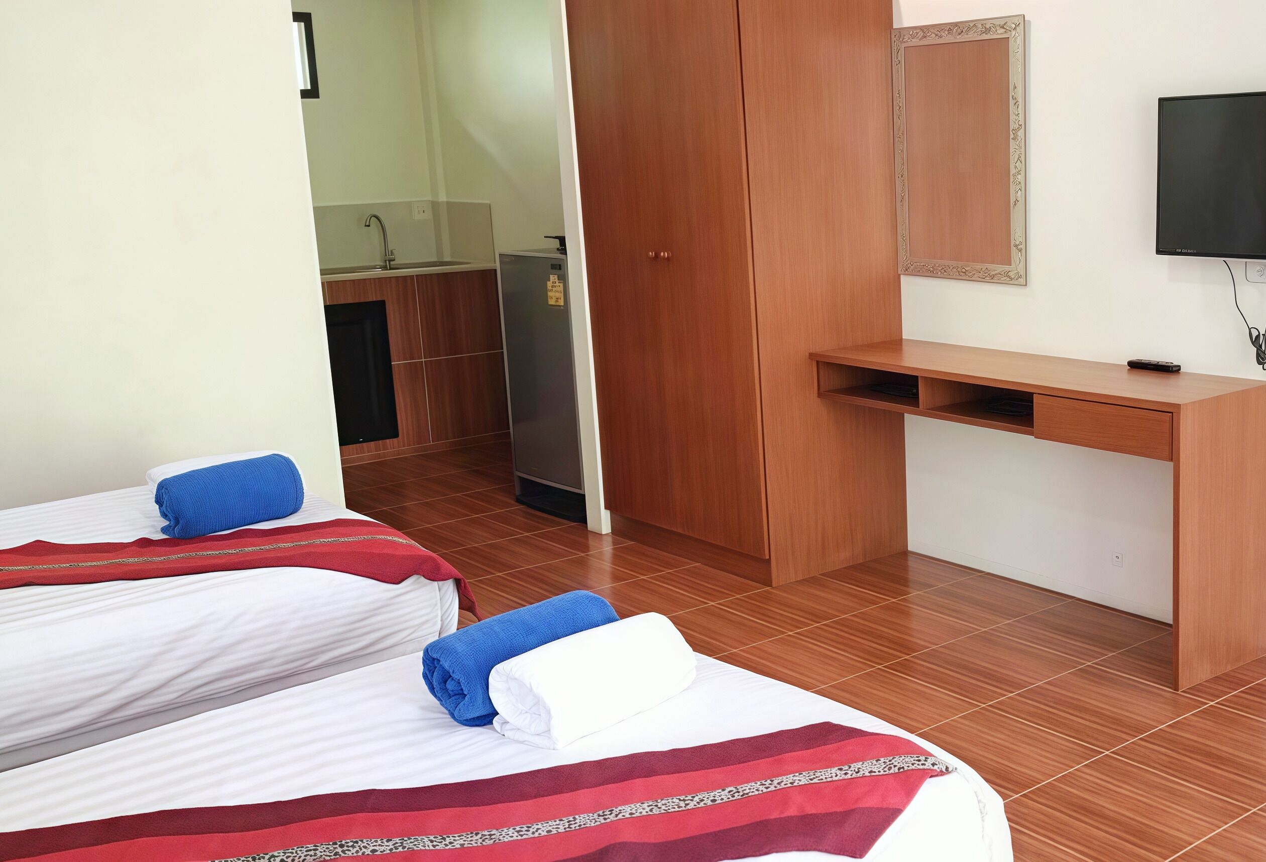 Een hotelkamer met twee bedden, een houten bureau, een televisie en een kitchenette.