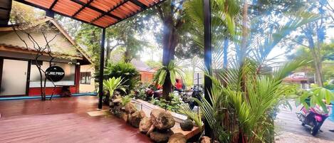Un espacio al aire libre cubierto con piso de madera, rodeado de plantas tropicales y un muro de piedra.