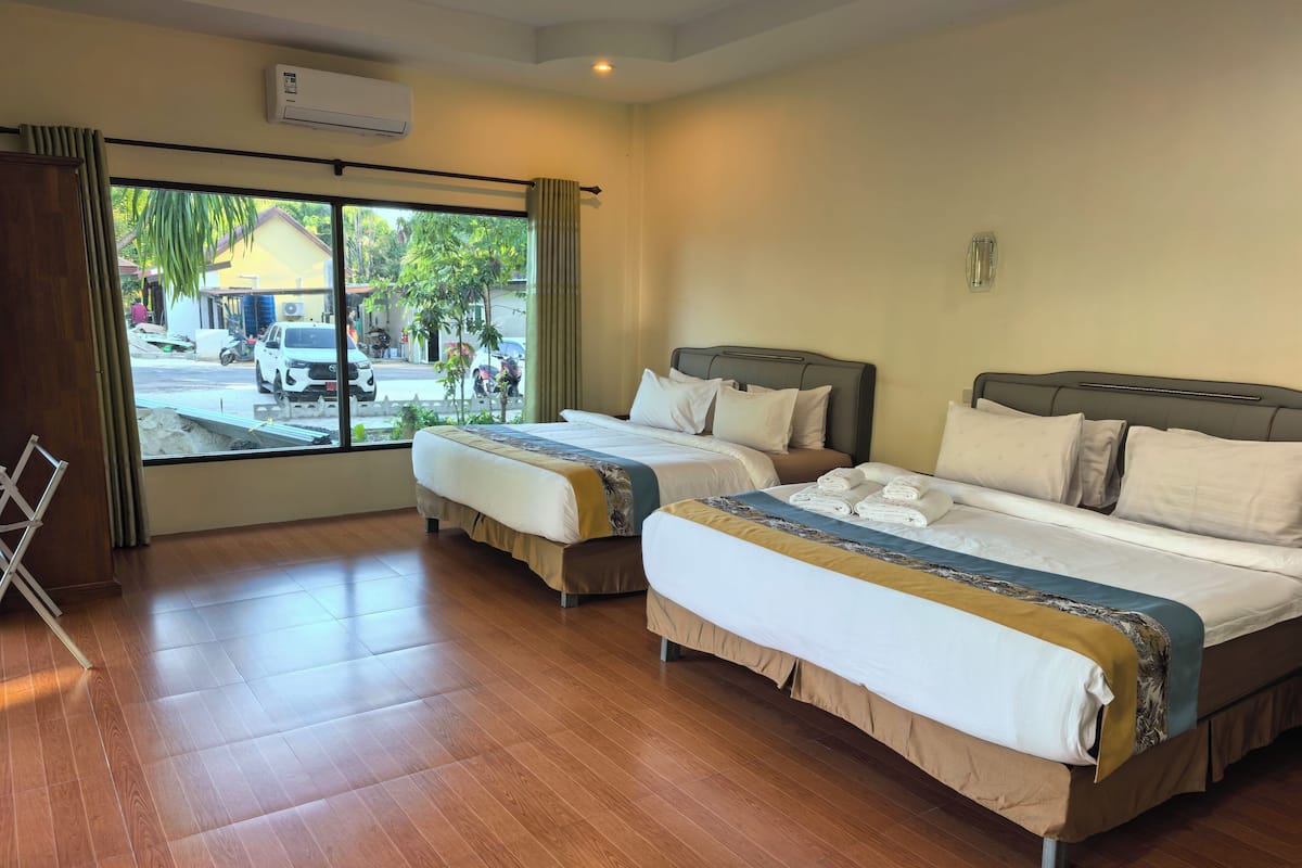 A hotel room with two beds, a window with a view of the street, and an air conditioning unit.