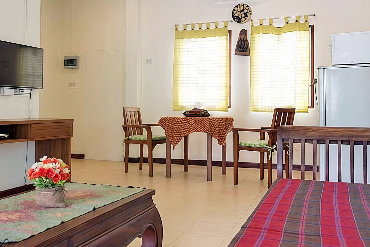 A dining area with a table set for two, a television, and a refrigerator.