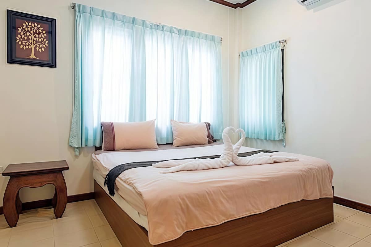 A neatly made bed with a pink bedspread and two pillows, a wooden nightstand, and a framed tree artwork on the wall.