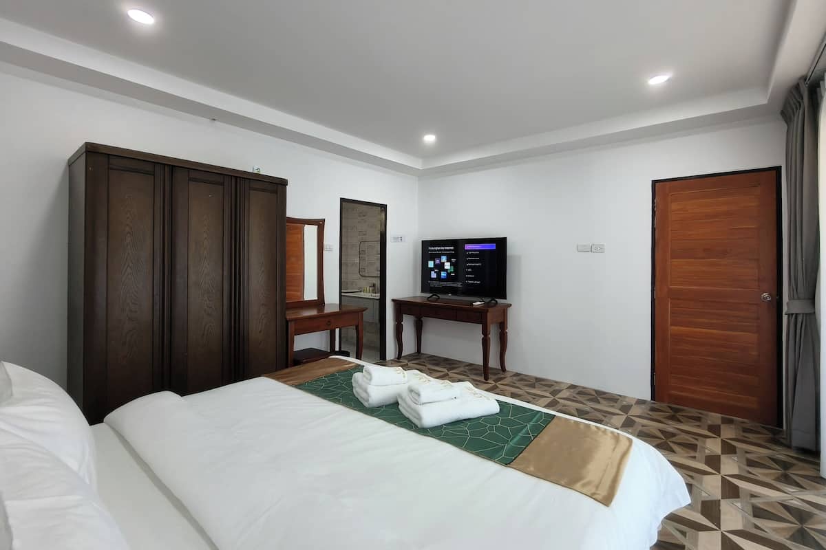 A hotel room with a bed, a wooden wardrobe, a desk with a computer, and a bathroom visible through a door.
