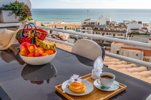 Une table avec un saladier de fruits, une assiette avec une pâtisserie et une tasse de café, le tout sur un balcon donnant sur la mer.