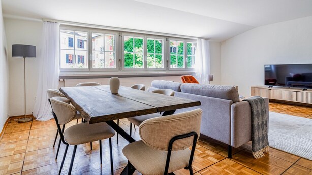 A modern living room with a dining area, large windows, and a flat-screen TV. - Blueground | Zurich town hall, city view, nr Rathaus (Zurich)