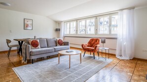 A modern living room with a grey sofa, a round coffee table, a red armchair, and a dining area with a table and chairs. - Blueground | Zurich town hall, city view, nr Rathaus (Zurich)