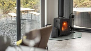 A modern interior with a wood-burning stove, a glass table, and a view of the outdoors.
