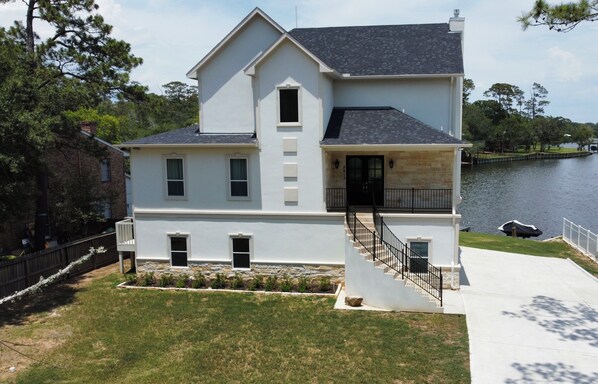 A two-story house with a front porch, a small front yard, and a dock by the water.