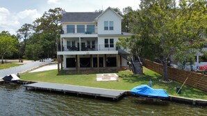 A two-story house with a balcony, a covered deck, and a dock extending into a body of water. - Waterfront Retreat Getaway with Gameroom Firepit Fishing Kayaks (Dickinson)