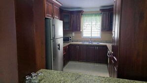 A kitchen with dark wooden cabinets, a stainless steel refrigerator, a microwave, and a granite countertop.