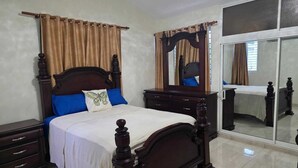 A bedroom with a wooden bed, a nightstand, a dresser, a mirror, and a sliding glass door.