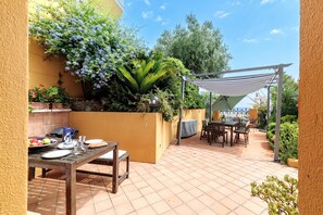 An outdoor patio with a table set for dining, surrounded by potted plants and a pergola providing shade.