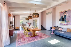 A spacious dining area with a long wooden table, multiple chairs, and hanging chandeliers.
