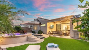 A backyard with artificial grass, a hot tub, and outdoor furniture. - KC Oasis POOL W/ HOT Tub Family fun for ALL (Gilbert)