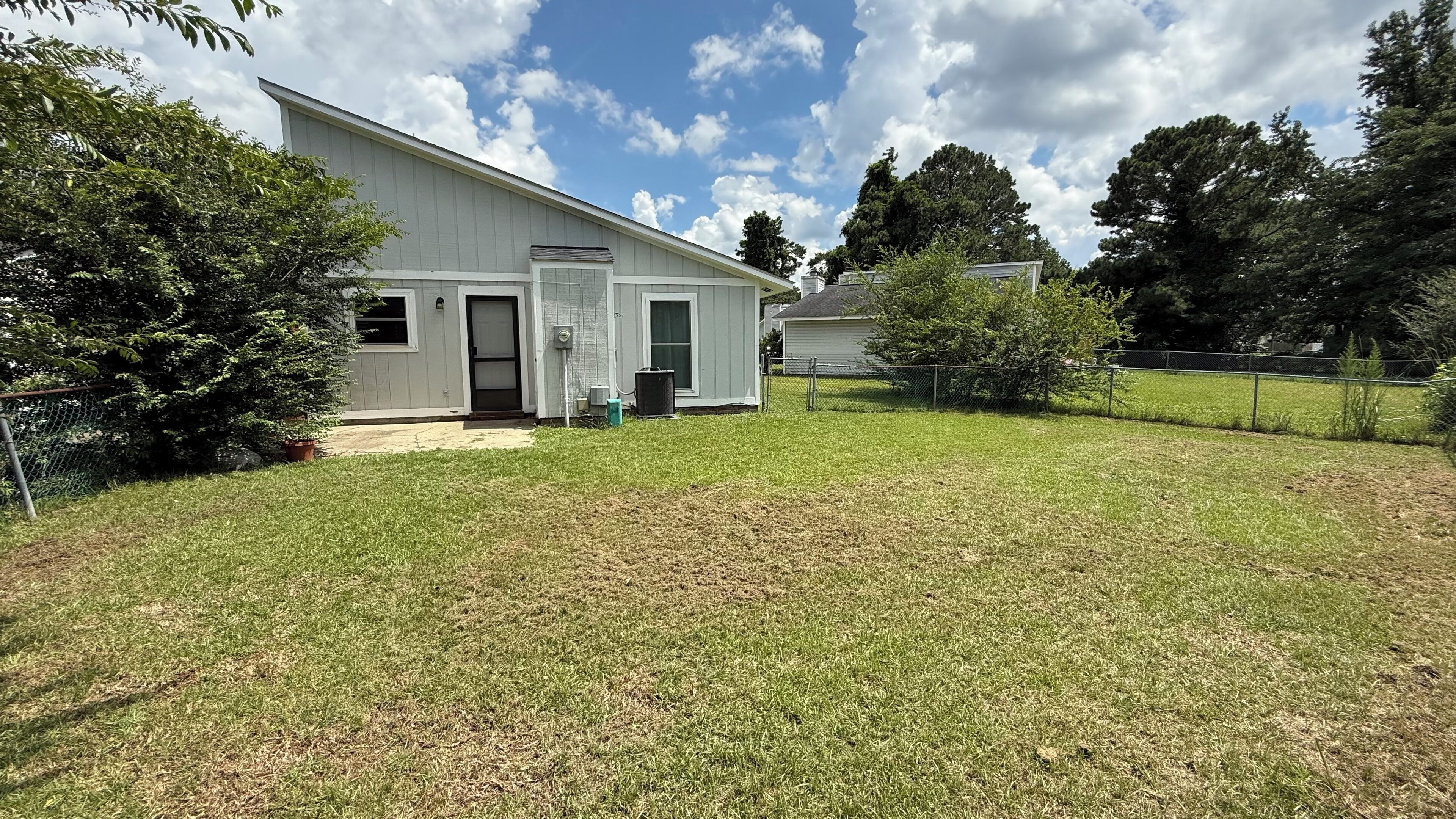 A single-story house with a front porch, a small front yard, and a chain-link fence.