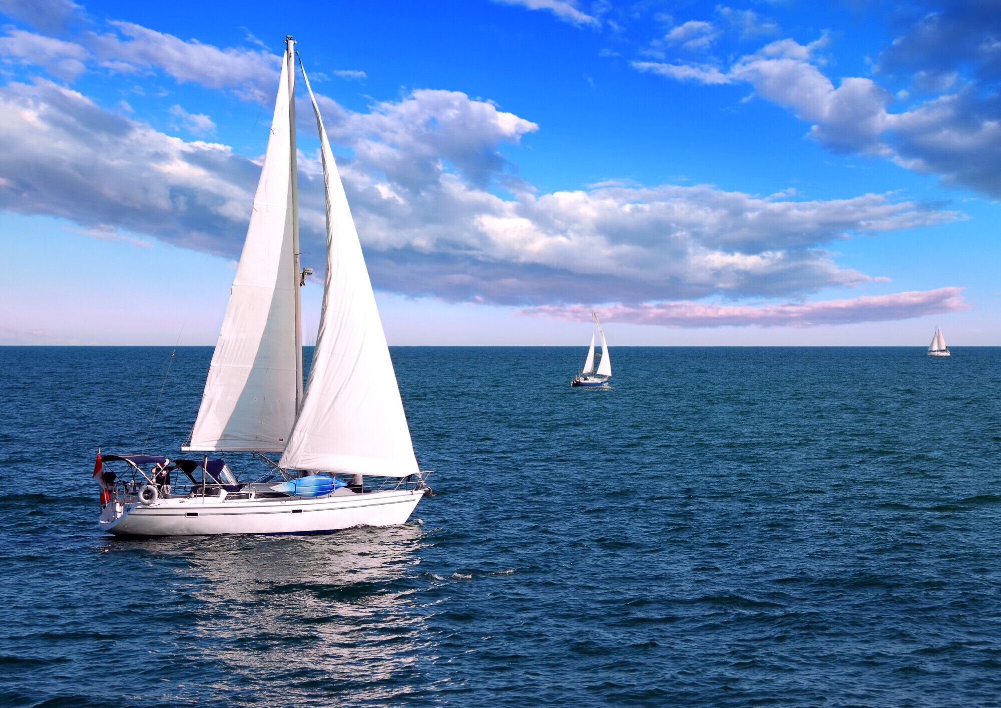 Een zeilboot op rustig water met een heldere lucht en zeilboten in de verte.