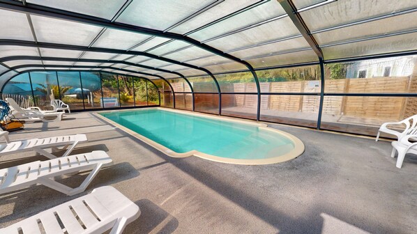 An indoor swimming pool with a glass ceiling, surrounded by white lounge chairs.