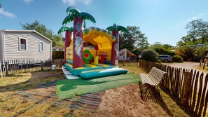 A backyard with a colorful inflatable play structure, a wooden bench, and a fenced area.