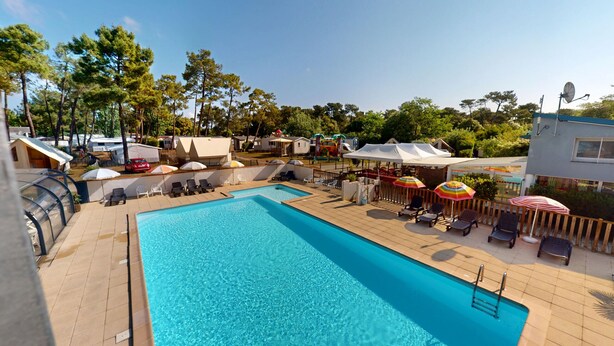 Une piscine entourée d’une terrasse et d’arbres, avec des chaises longues et des parasols.