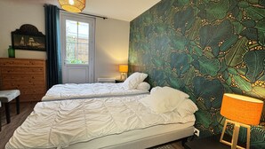 A bedroom with two beds, a dresser, a window with curtains, a wall with a leafy pattern, and a lamp.