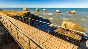 A coastal walkway with a metal railing, rocky outcrops, and the sea.
