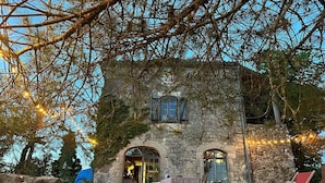 A stone building with arched windows and a stone wall in front. There are outdoor seating areas with cushions and a table.