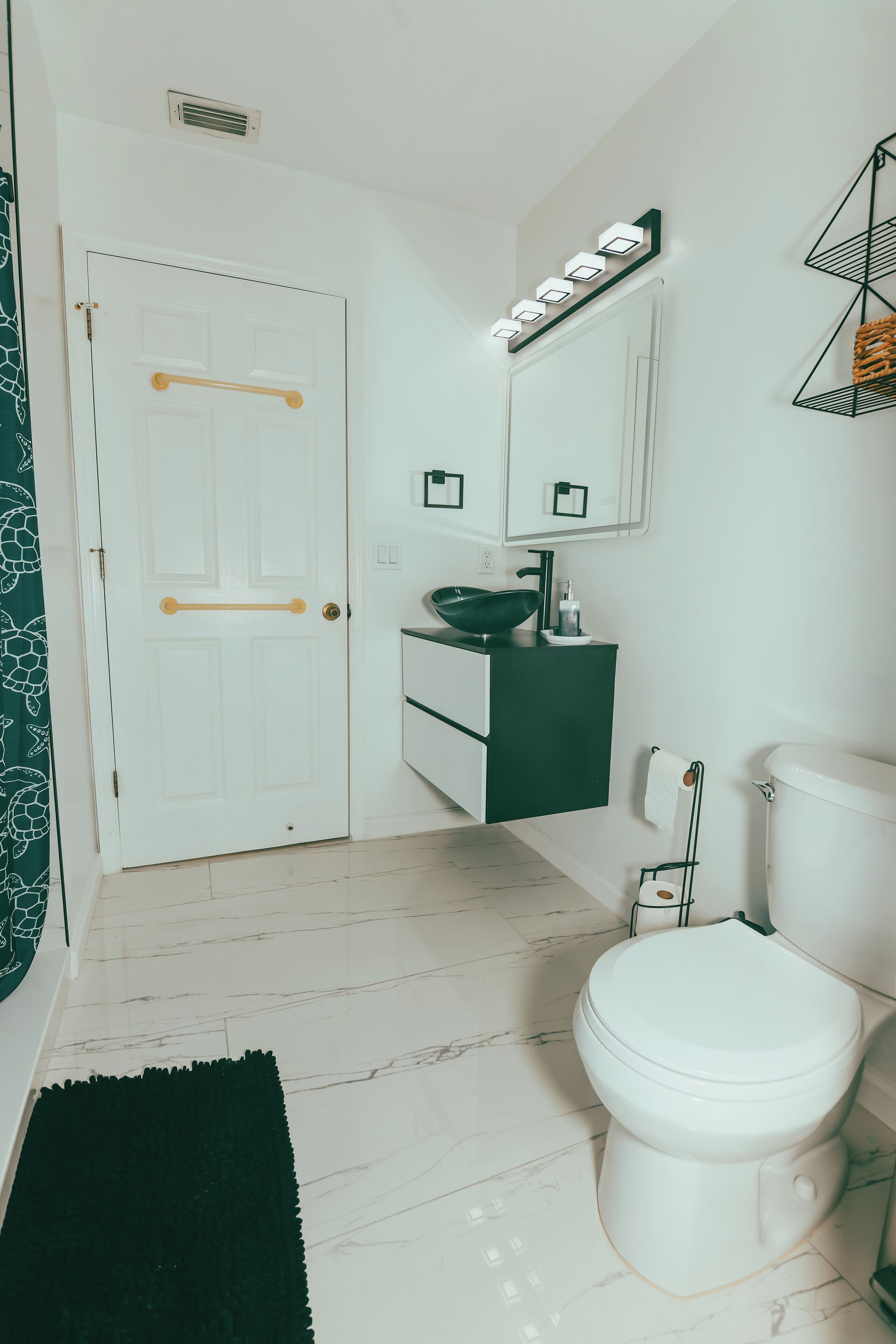 Un baño moderno con inodoro blanco, lavabo verde y puerta blanca con un perchero.