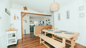 A wooden dining table with benches, a kitchen area, and a white interior.