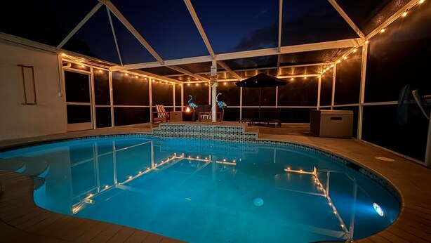 An indoor swimming pool with a glass floor, surrounded by a covered deck with string lights and seating areas.