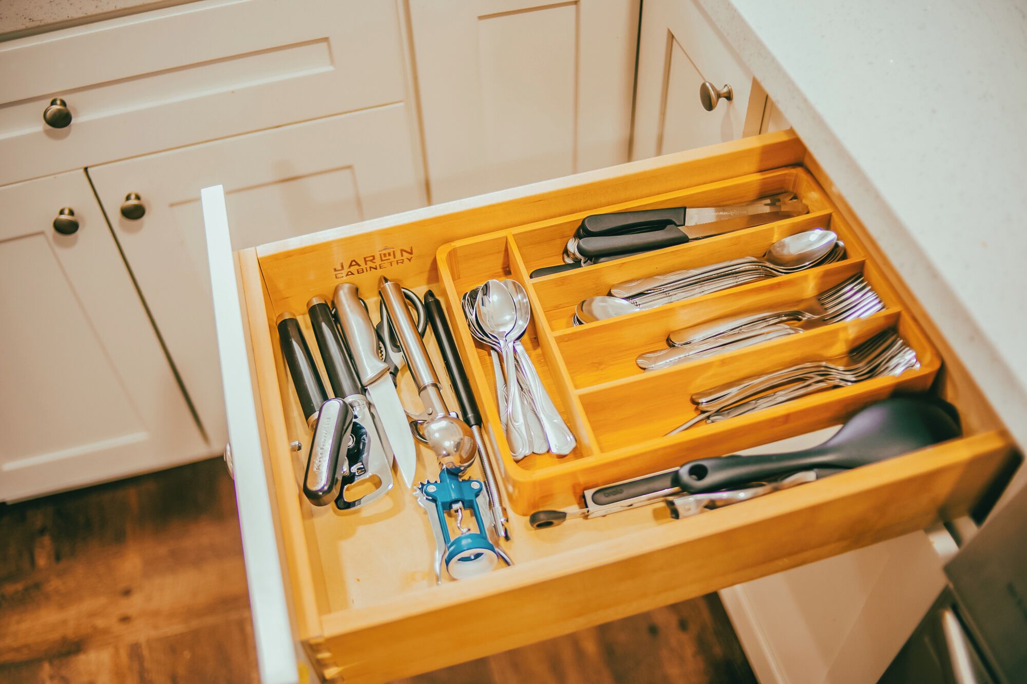 A kitchen drawer with utensils and tools, including knives, spoons, and a can opener.