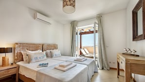 A bedroom with two beds, a wooden headboard, a bedside table with a lamp, a desk, and a view of the outside. - Cabanas Gardens, 4px, Penthouse (Cabanas de tavira)