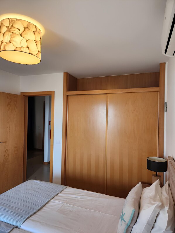 A bedroom with a bed, a wooden wardrobe, a hallway, and a lamp.