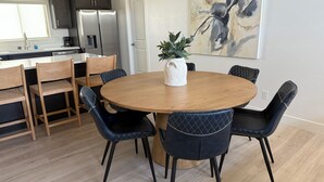 Una cocina moderna con armarios oscuros, un refrigerador de acero inoxidable y un comedor con una mesa redonda de madera y sillas tapizadas en negro.