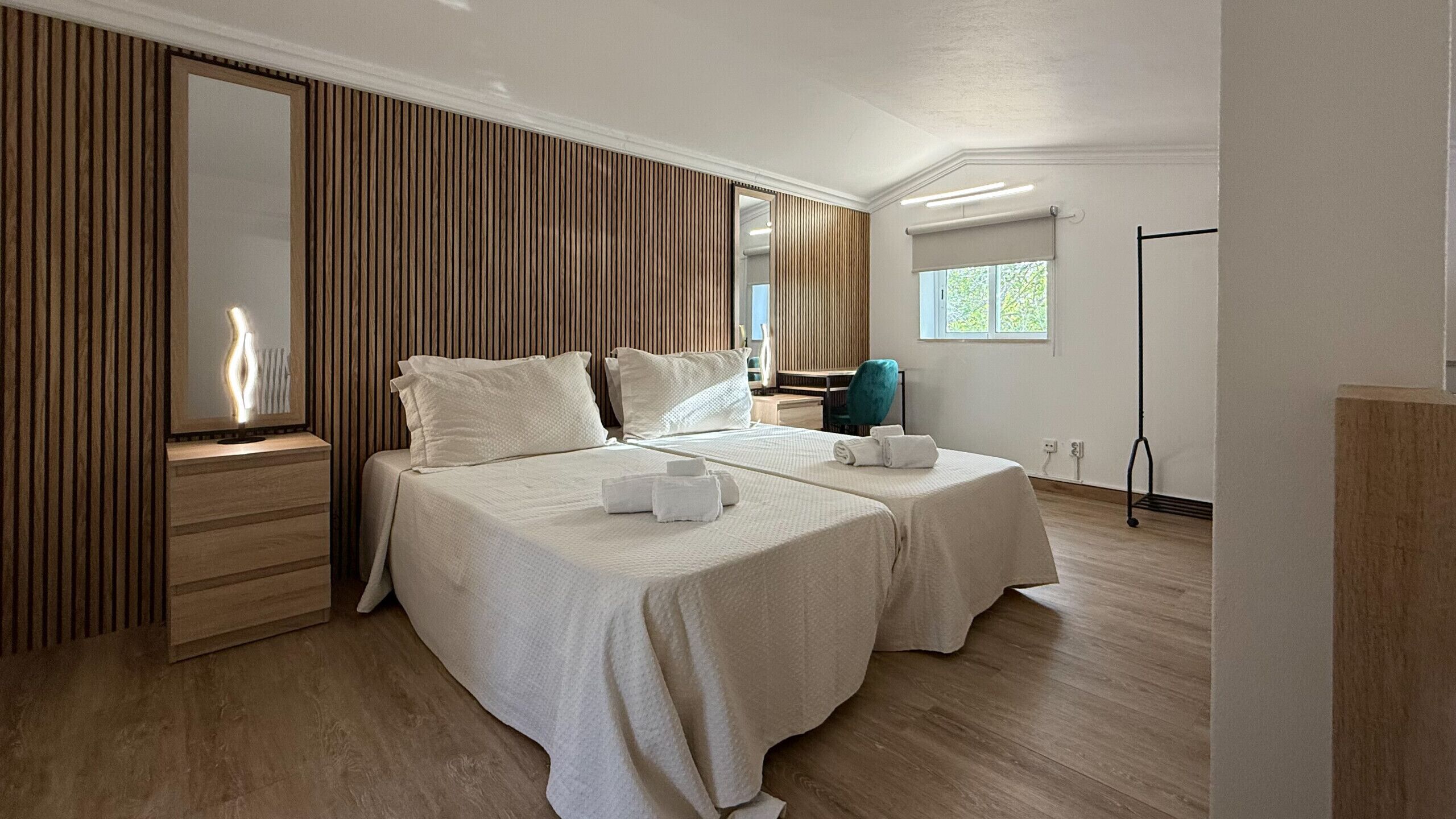 Une chambre d’hôtel avec deux lits, un grand miroir, un mur recouvert de panneaux de bois, une fenêtre et un lampadaire.
