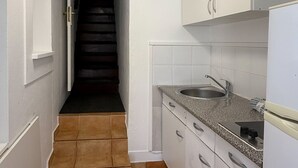 A narrow kitchen with white cabinets, a stainless steel sink, and a tiled floor.