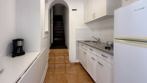 A narrow kitchen with white cabinets, a coffee maker, a sink, and a refrigerator.