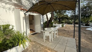 A patio with a table and chairs under a canopy, a door leading to a kitchen, and a landscaped garden with trees and shrubs.