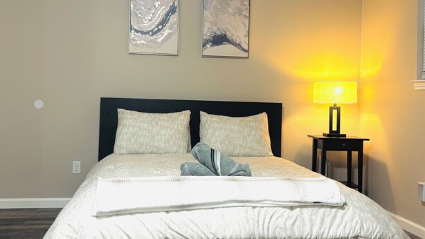 A neatly made bed with a white comforter and pillows, a bedside table with a lamp, and two abstract art pieces on the wall. - Charming cozy studio in Austin (Austin)