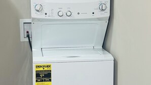 A front-loading white washer and dryer unit with a yellow ENERGY GUIDE sticker, located in a room with wooden flooring and beige walls. - Charming cozy studio in Austin (Austin)