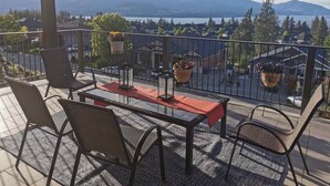 Ein Balkon mit Tisch, Stühlen, hängenden Pflanzgefäßen und Blick auf Berge und See.